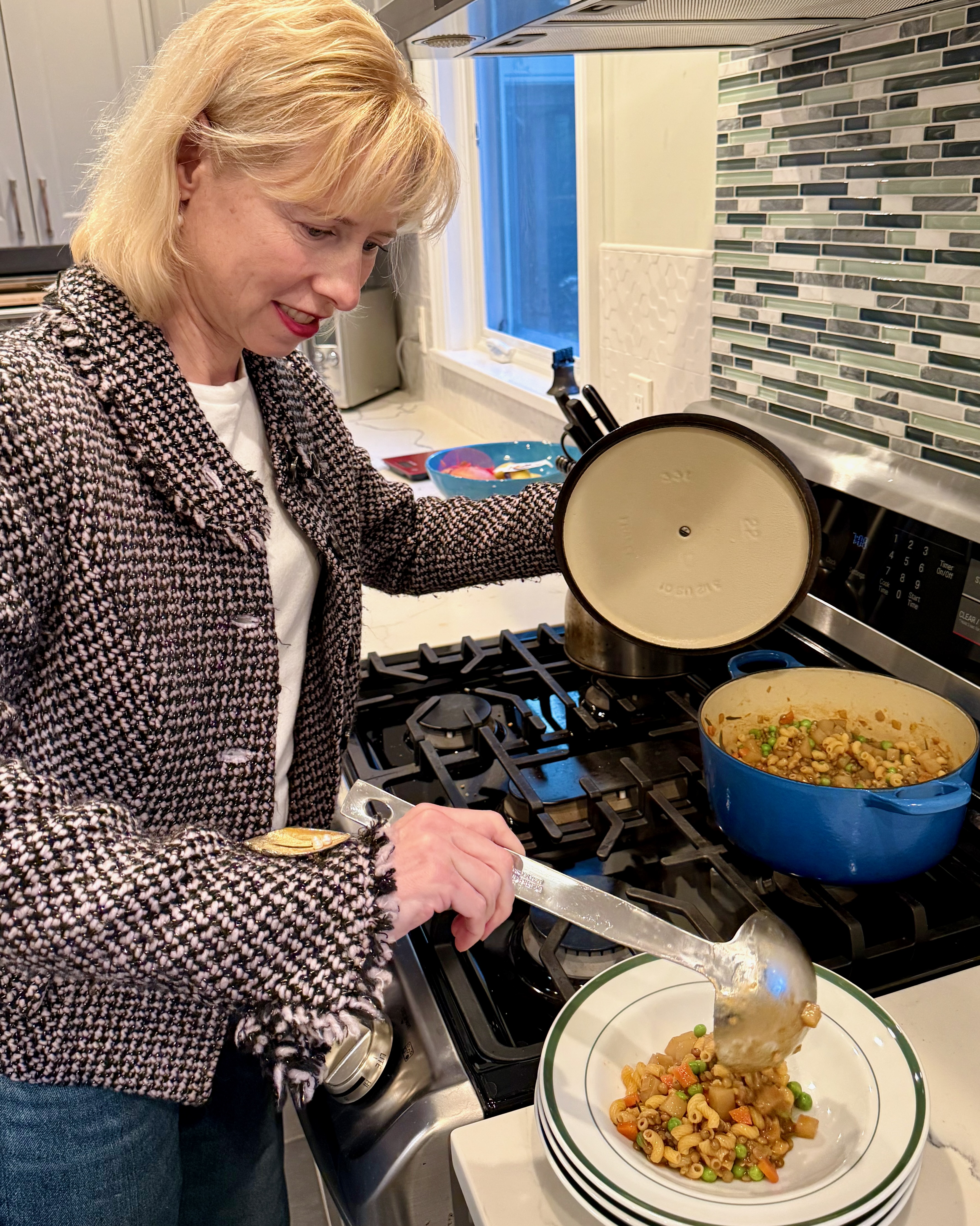 A woman ladles a hearty-looking pasta and lentil dish from a pot into a bowl