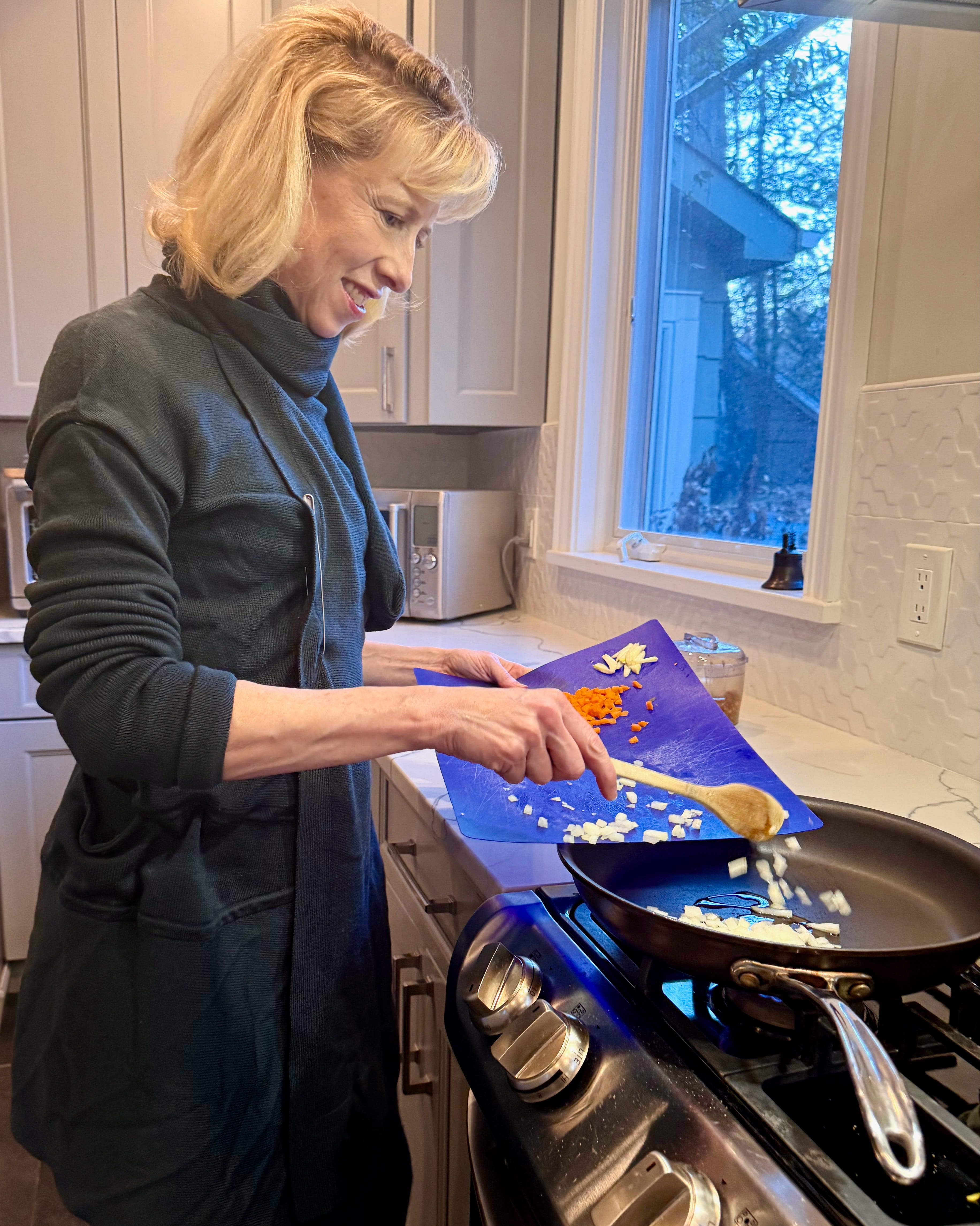 A woman scrapes chopped vegetables into a skillet on a stove